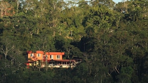 A two-story building with a red roof, surrounded by dense forest. - Hostal Tena Ñaui (Tena)