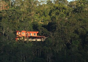 Un edificio de dos pisos con techo rojo, rodeado de un bosque frondoso.