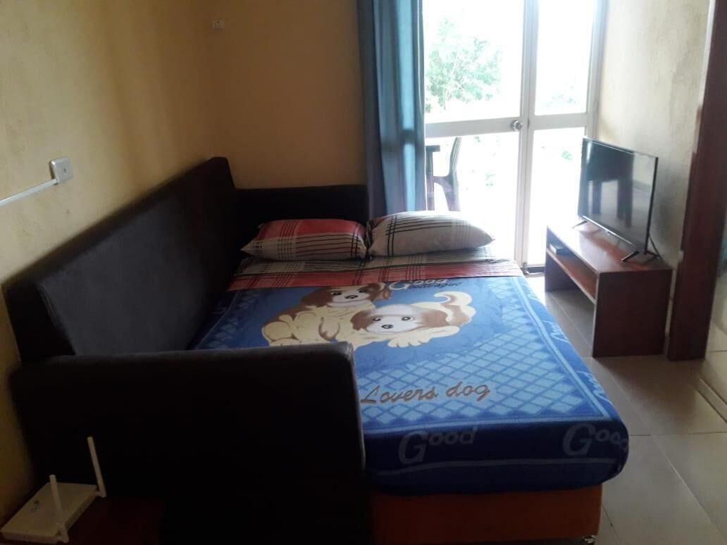 A bedroom with a bed, a TV on a stand, and a window with curtains.