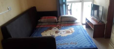 A bedroom with a bed, a TV on a stand, and a window with curtains.