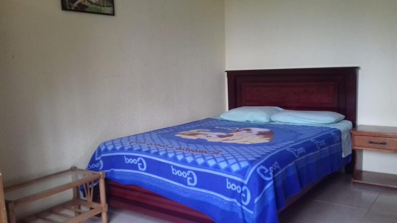 Ein Schlafzimmer mit einem Bett, das mit einer blauen Decke bezogen ist, einem Holzkopfteil, einem Nachttisch und einem kleinen Holzstuhl.