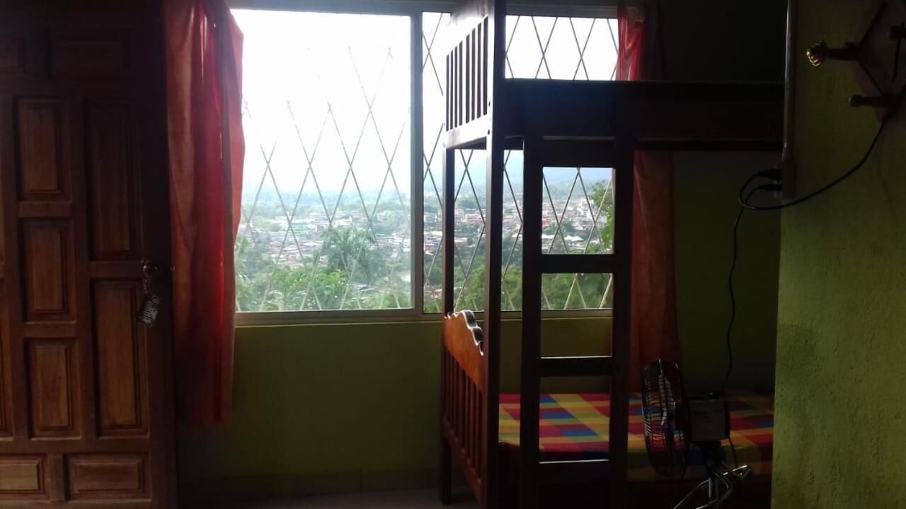 A room with a window overlooking a cityscape, a bunk bed, and a small table with a fan.