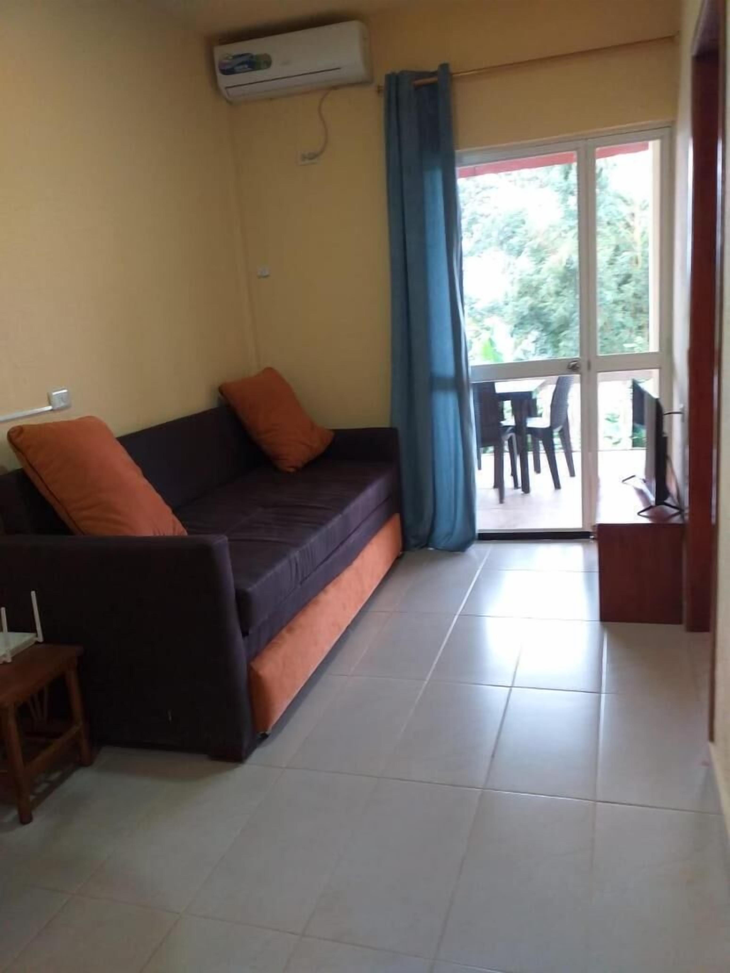 A compact living space with a sofa, a small table, and a sliding glass door leading to an outdoor area with a table and chairs.