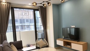 A modern living room with a sofa, a round coffee table, a TV on a wooden stand, and a balcony with a view of the city.