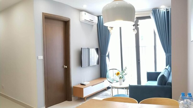 A modern living room with a wooden dining table, a sofa, a TV, and a large window with curtains.