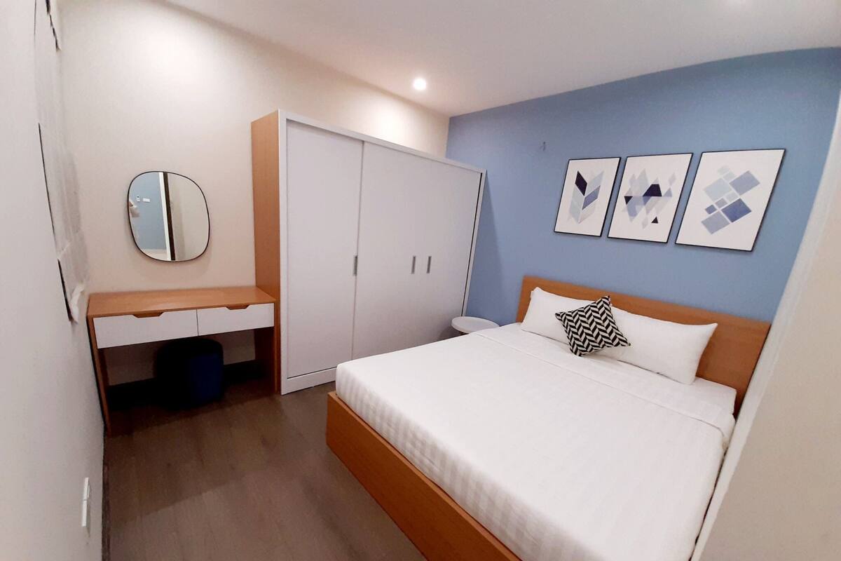 A bedroom with a bed, a wardrobe, a desk, and a mirror.