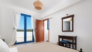 A bedroom with a bed, a desk, a chair, a mirror, and a door leading to a balcony. - Blue Moon Villa in Kolympia (RHODES)