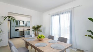 A modern dining area with a wooden table, grey chairs, and a bowl of green apples. - Blue Moon Villa in Kolympia (RHODES)
