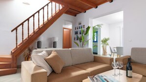 A living room with a sofa, a coffee table with a magazine and wine glasses, a staircase, and a door leading to another room. - Blue Moon Villa in Kolympia (RHODES)