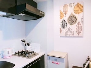 A kitchen with a gas stove, a kettle, and a microwave. There is a wall-mounted artwork of leaves.
