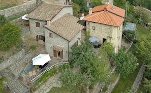 A stone house with a tiled roof, a patio with outdoor furniture, and a garden area. - Canto del fiume, Raggiolo, Tuscany, surrounded by nature  (RAGGIOLO)