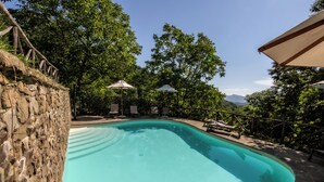 A swimming pool with stone walls and lounge chairs, surrounded by trees and a stone deck. - Canto del fiume, Raggiolo, Tuscany, surrounded by nature  (RAGGIOLO)