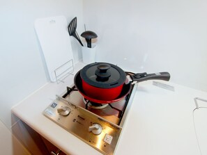 A kitchen with a red pot on a gas stove, a white refrigerator, and a set of kitchen utensils on the wall.