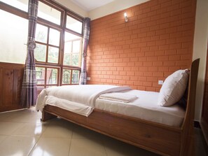 A single bed with a wooden frame, a brick wall behind it, and a window with curtains. - Kakakuona Resort (Lushoto)