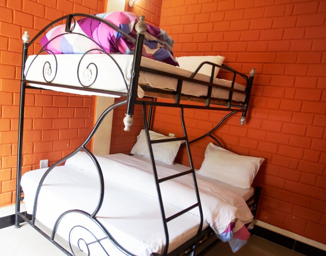 A bunk bed with white bedding and a metal frame, set against a brick wall.