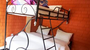A bunk bed with white bedding and a metal frame, set against a brick wall.