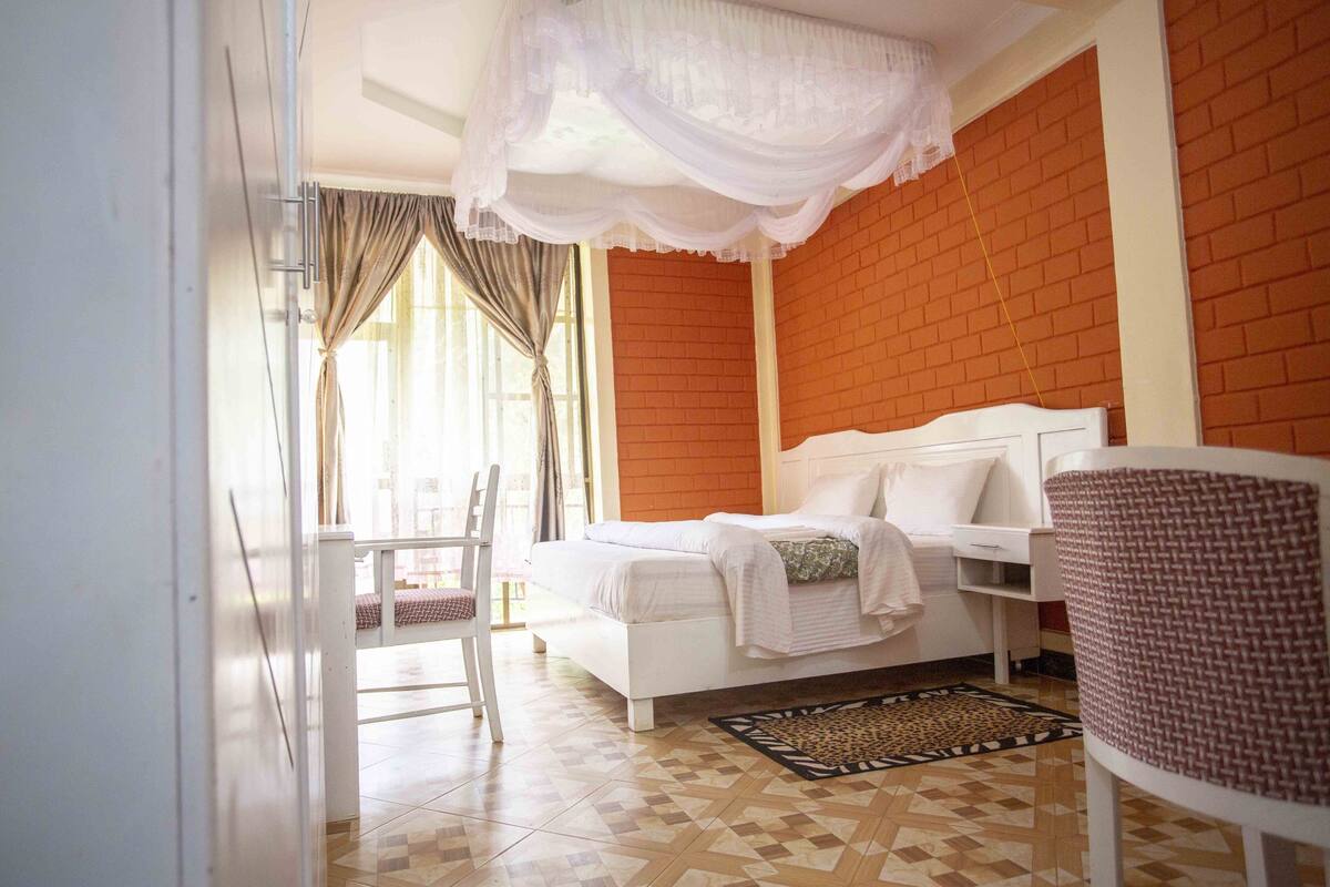 Un dormitorio con cama blanca, pared de ladrillo rojo y suelo estampado.