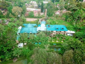 An aerial view of a large, multi-story building with a central dome and multiple wings, surrounded by lush greenery and a small pond. - Kakakuona Resort (Lushoto)