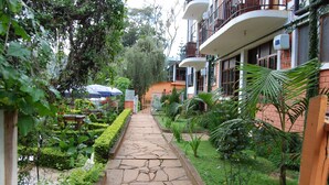 A pathway leading to a building with balconies, surrounded by lush greenery and a well-maintained garden.