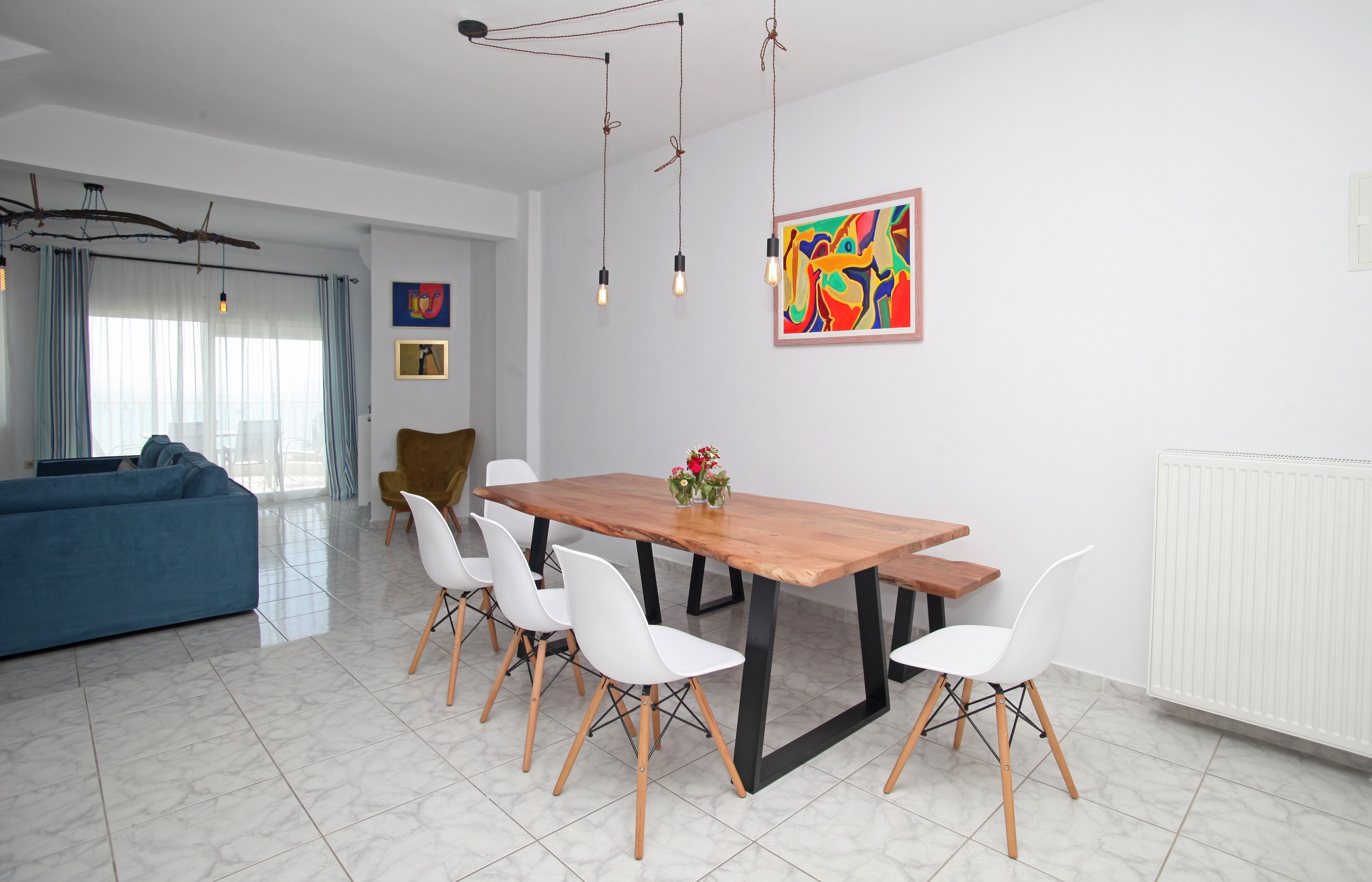 Een moderne eetruimte met een houten tafel, witte stoelen en een kleurrijk abstract schilderij aan de muur.