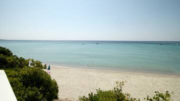 Une plage à l’eau turquoise et limpide, un rivage sablonneux et quelques bateaux visibles au loin.