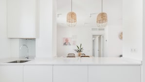 A modern kitchen with white cabinets, a stainless steel sink, a hanging wicker light fixture, and a small potted plant on the counter.