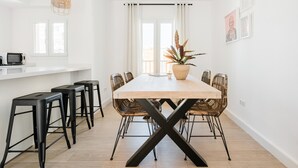 A modern dining area with a long table, black bar stools, wicker chairs, and a potted plant.