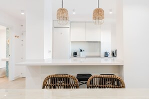 Une cuisine moderne avec des meubles blancs, une cuisinière encastrée et deux chaises en osier.