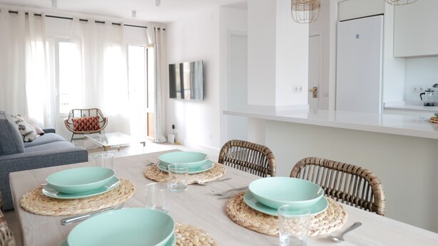 A modern dining area with a wooden table set for four, surrounded by wicker chairs.