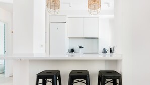 A modern kitchen with white cabinetry, a white countertop, and three black stools.