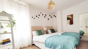A modern hotel room with a large bed, a bedside table, a lamp, a shelf with books, and a wall with bird decorations.