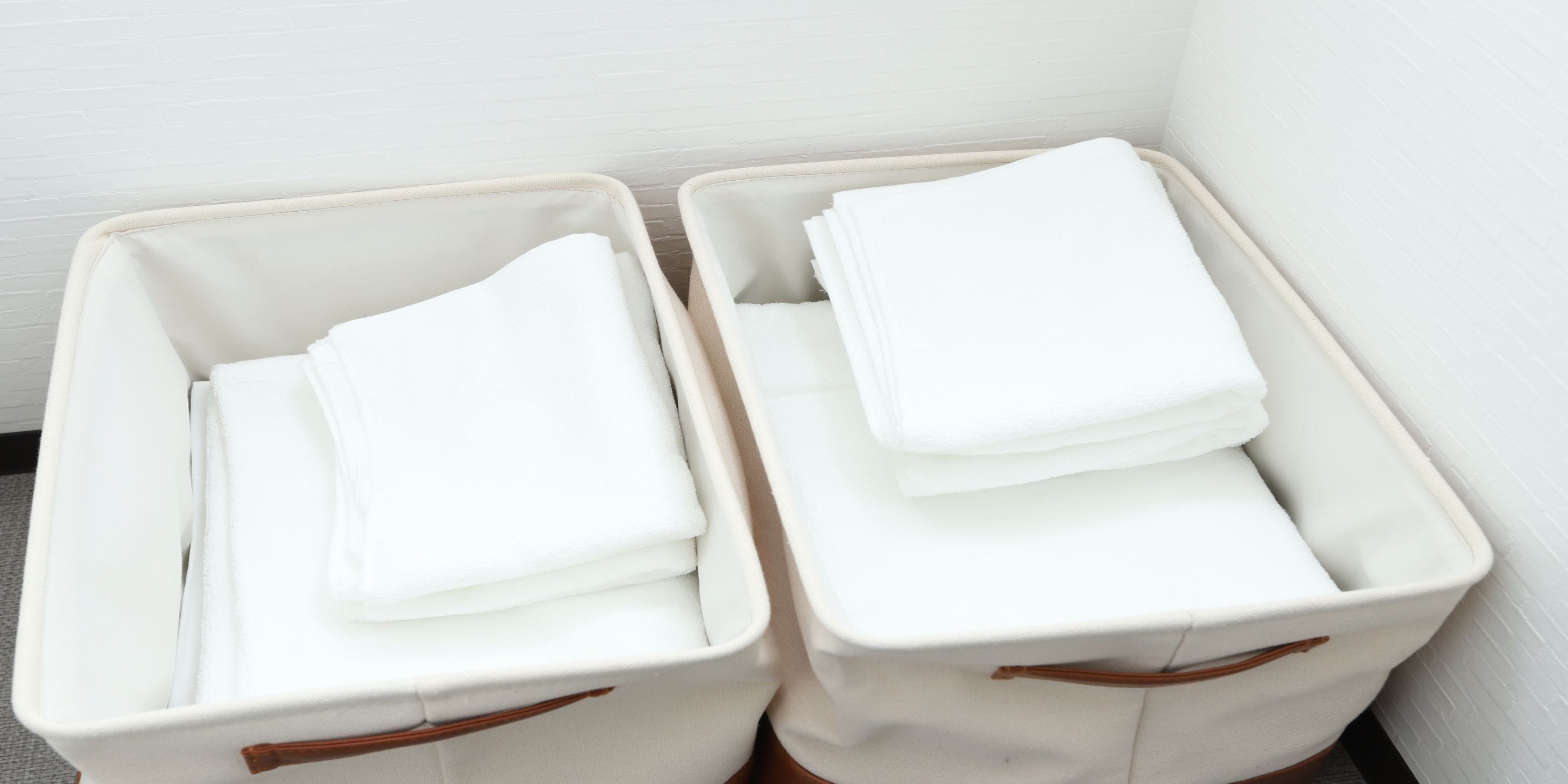 Two white storage bins with handles, stacked with folded white towels.