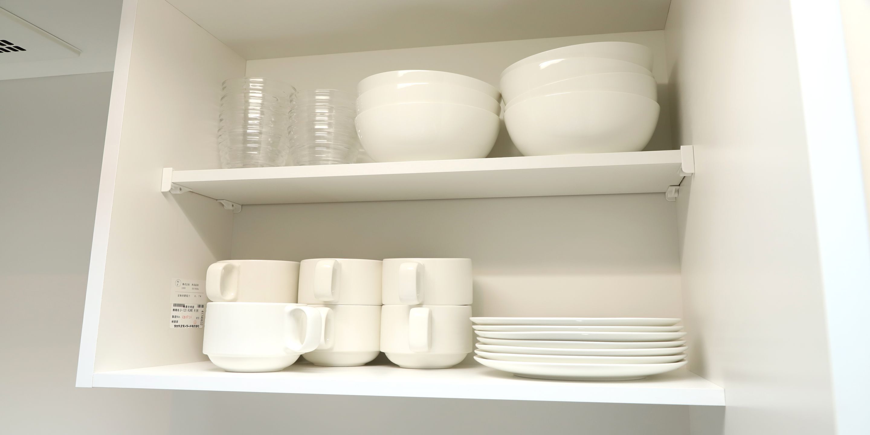 A white interior with shelves holding white cups, bowls, and plates.