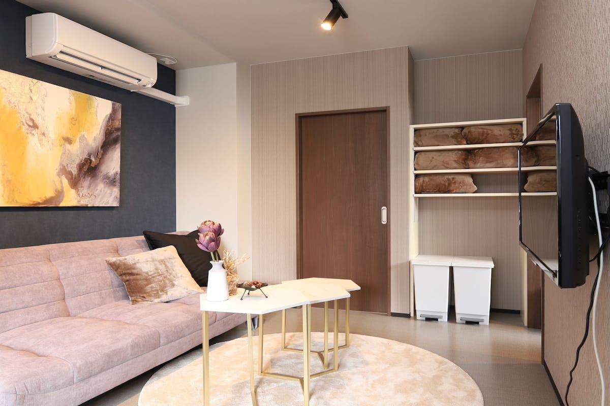 A modern living room with a sofa, a coffee table, a flat-screen TV mounted on the wall, and a built-in shelving unit.