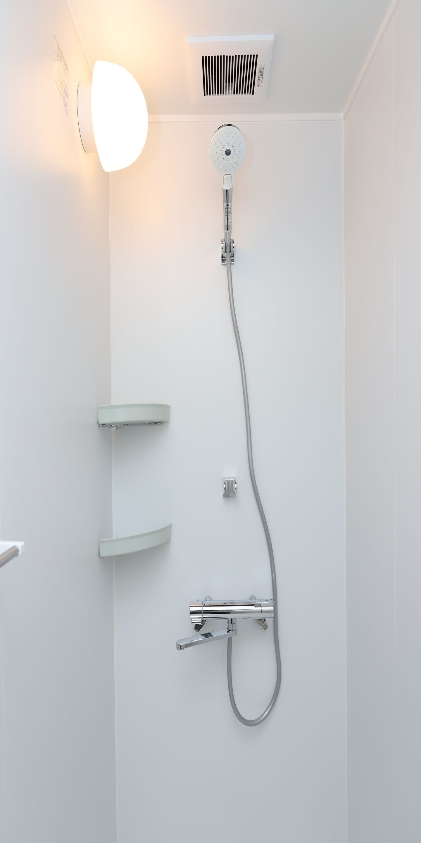A modern shower with a handheld showerhead, a wall-mounted control panel, and a light fixture above the shower.