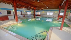 Une piscine intérieure avec un plafond en bois, une eau cristalline et un sol carrelé.