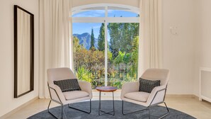 Ein Zimmer mit zwei Sesseln, einem kleinen runden Tisch und Bergblick durch ein großes Fenster.