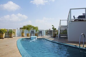 En pool på taget med klar blå himmel, træterrasse og plantekrukker.
