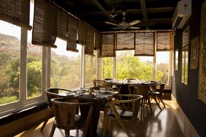 Un coin repas avec une table dressée pour quatre personnes, de grandes fenêtres et un ventilateur de plafond.