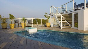Une piscine sur le toit, agrémentée d’une terrasse en bois, de plantes en pot et de meubles pour se détendre en plein air.