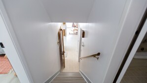 A narrow staircase with a handrail, leading to a room with a tiled floor and a door at the top. - Central, 2 bedroom King/Queen, Semidetached House in French Quarter (Edmonton)