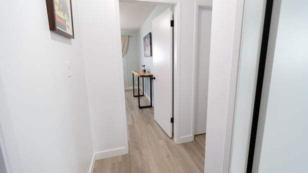 A narrow hallway with white walls and wooden flooring. There is a framed picture on the left wall and a small table with a vase in the distance. - Central, 2 bedroom King/Queen, Semidetached House in French Quarter (Edmonton)