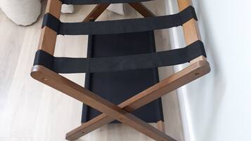 A wooden chair with black straps and a black cushion, positioned against a wall.