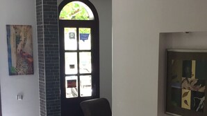 A hallway with a tiled floor, a patterned rug, a black door with a window, and a framed picture on the wall. - Sevgi Hotel Kalkan (Kas)