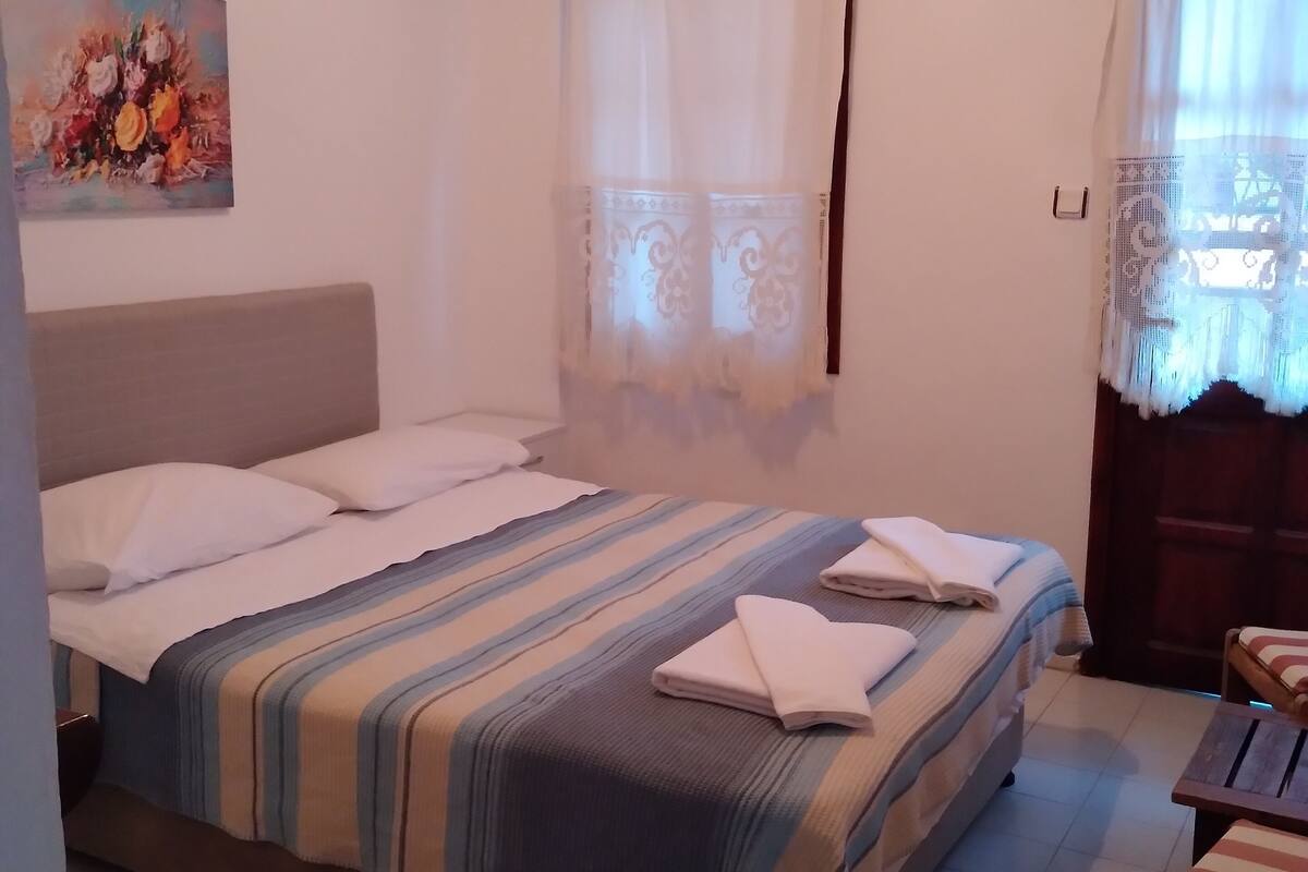 A neatly made bed with striped bedding and towels, a painting on the wall, and a patterned rug on the floor.