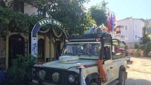 A vehicle with a sign reading "SEVGİ HOTEL" parked in front of a building with a stone wall and a flag. - Sevgi Hotel Kalkan (Kas)