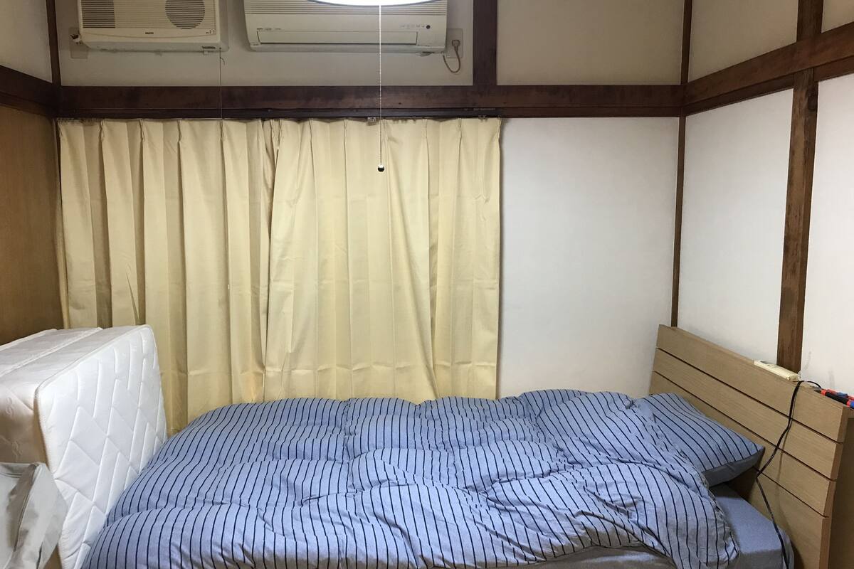 A room with a bed, a window with curtains, and an air conditioning unit.