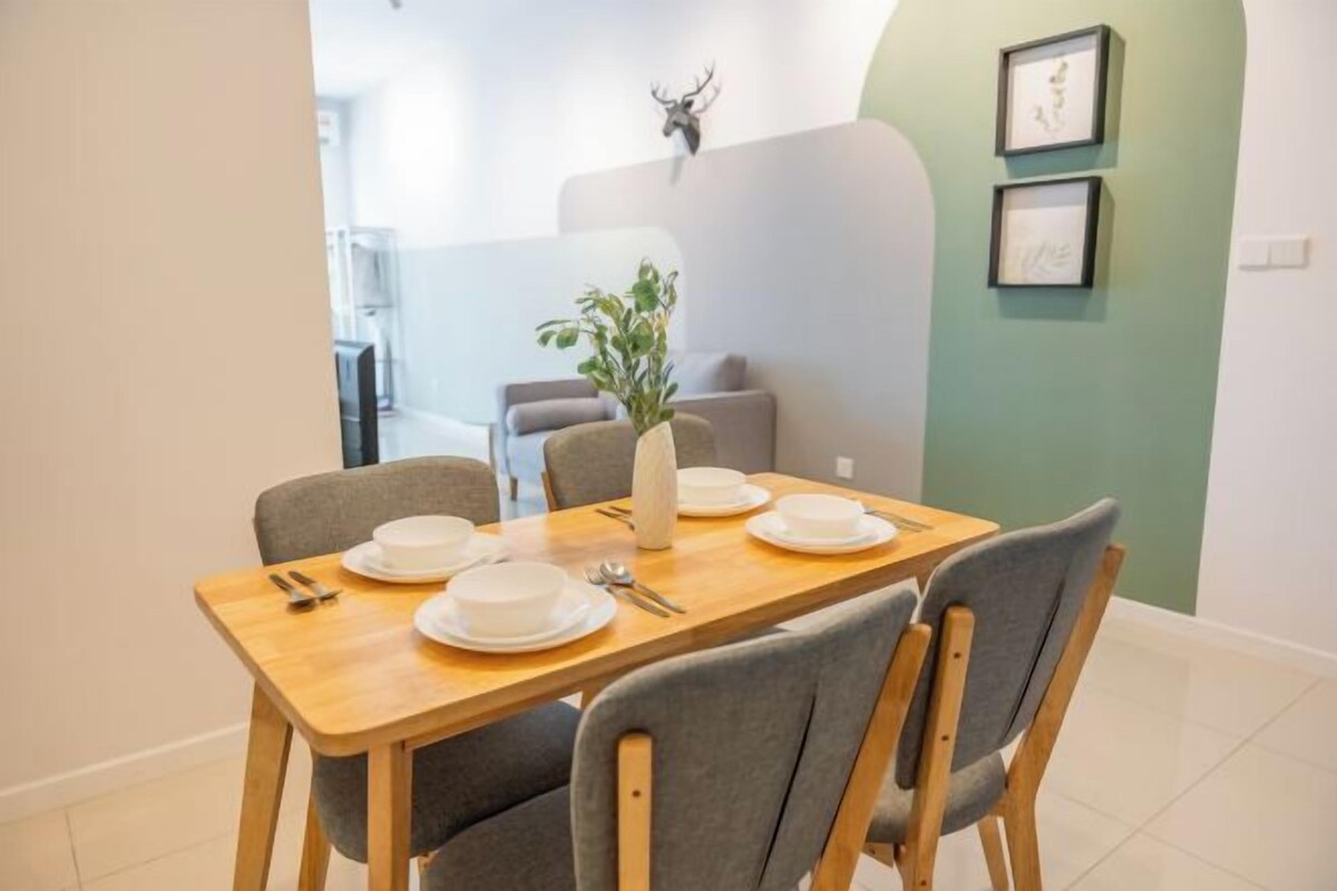 A dining area with a wooden table set for four, grey upholstered chairs, a vase with green plants, and a wall-mounted deer head decoration.