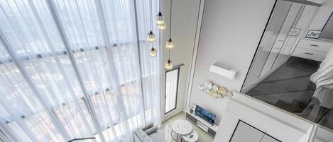 A modern hotel room with a large window, a sofa, a small round table, and a TV.