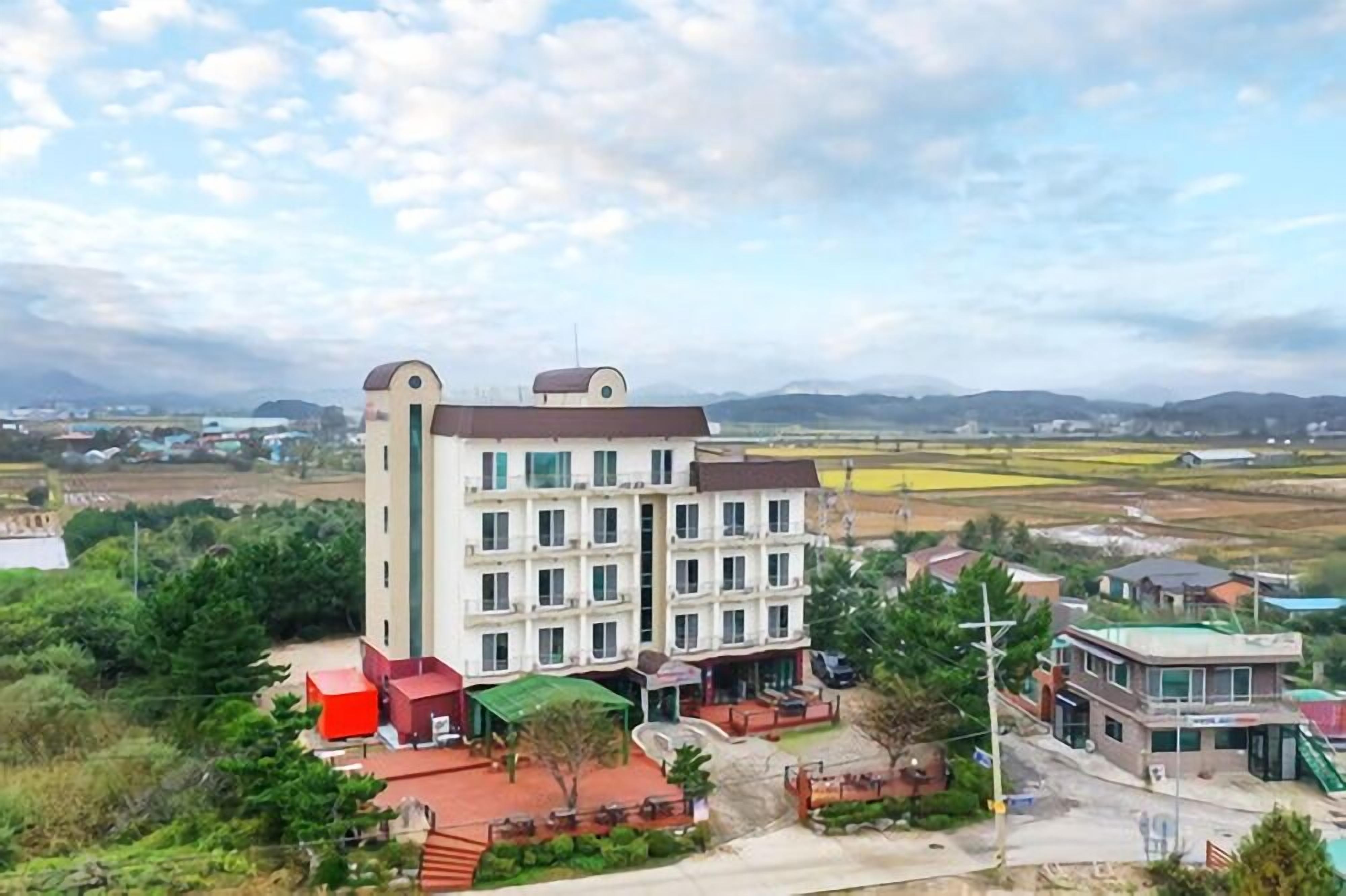 A multi-story hotel with a central courtyard, surrounded by greenery and a view of distant hills.